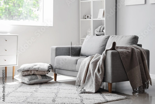 Fototapeta Cozy grey sofa with modern laptop in interior of light living room