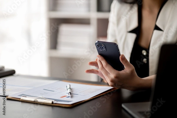 Fototapeta Beautiful asian woman looking at data on phone, businesswoman working in office attentively to grow and modernize start-up business, she is analyzing company's market and financial data.