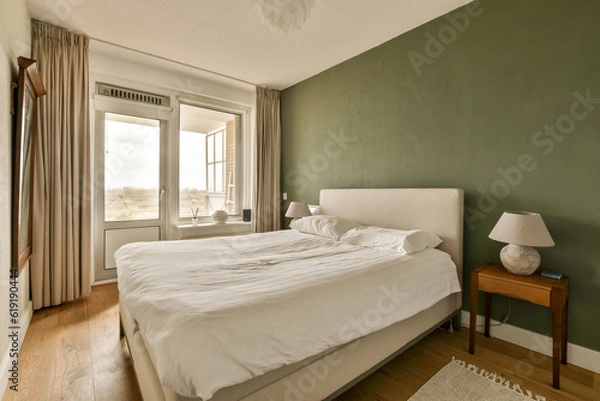 Obraz a bedroom with green walls and white bedding, wooden flooring and large windows overlooking the cityscapea