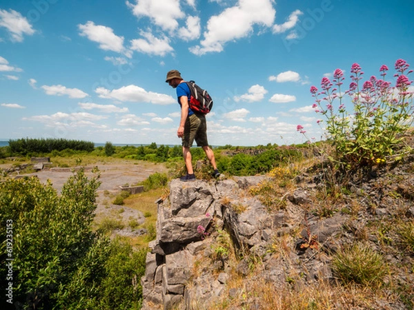 Fototapeta Slim athletic man on edge of a cliff, beautiful nature scene on a warm sunny day. Outdoor activity. Get out of town and adventure concept. Blue cloudy sky. Be active theme