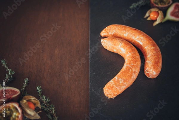Fototapeta Delicious chipolata sausages on a slate and wooden background. Raw meat prepared for cooking. Black slate / wood background. Space for text