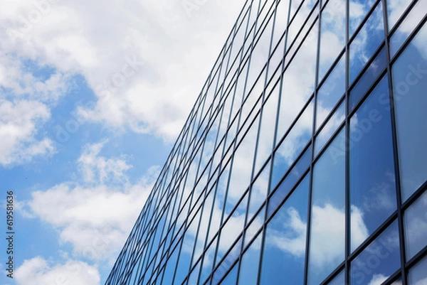 Fototapeta Construction of a glass facade structure. Modern office building, glass and clouds, real-estate investing concept. Place for text, business center with a glass facade. 