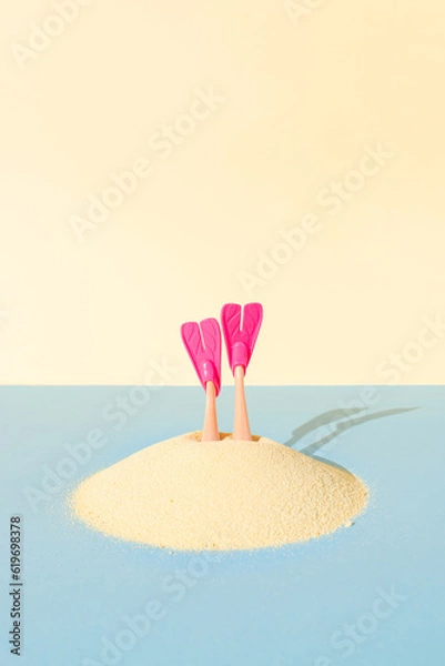 Fototapeta A pair of diving fins pokes out of the sand on blue and yellow pastel background. Creative idea of summer swimming recreation, or undersea vacation concept.