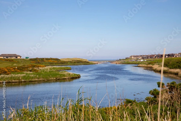 Fototapeta The river Ugie looking towards the town of Peterhead and the village of Buchanhaven on the right with the golf club and golf course on the left. A bridge and the sea are in the distance.