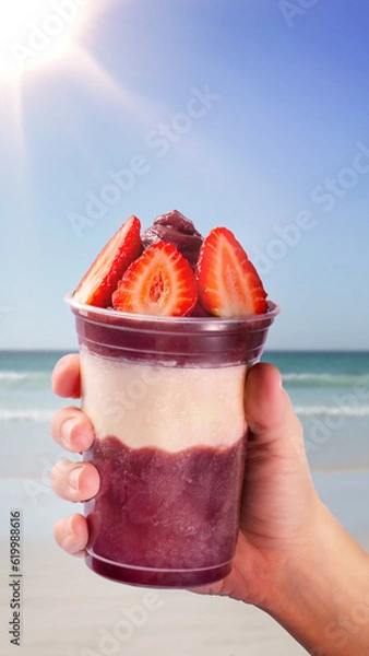 Fototapeta Hand holding a cup of açaí on the beach