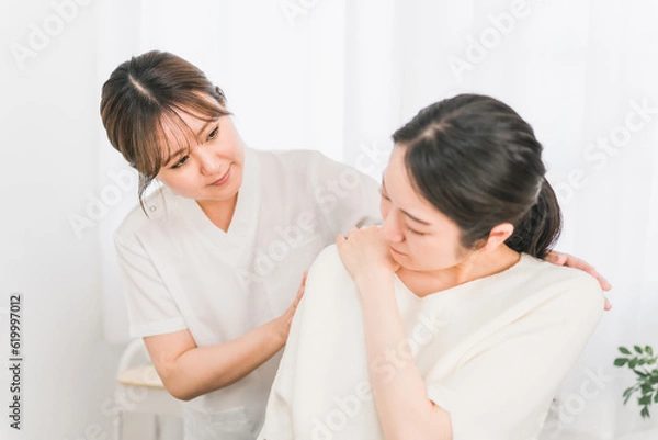 Fototapeta 整体院・整骨院に肩こり・リウマチの治療にきた患者と整体師・マッサージ師・セラピスト・医師の女性
