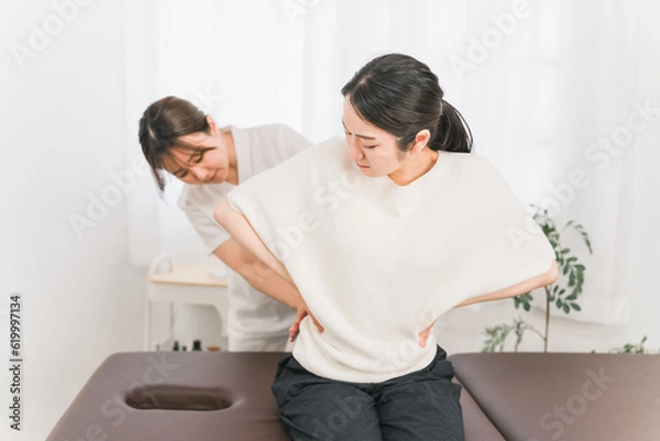 Fototapeta 整体院・整骨院に腰痛の治療にきた患者と整体師・マッサージ師・セラピスト・医師の女性
