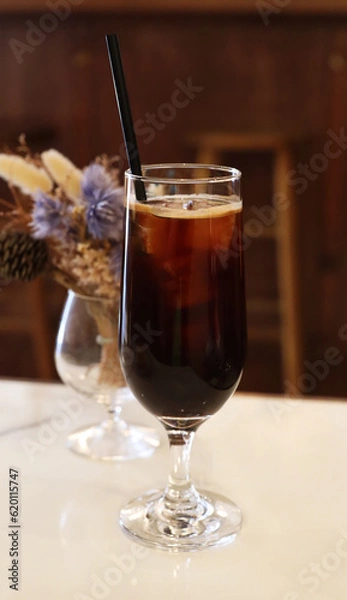 Fototapeta iced americano in the tall glass with flower vase behide on the table