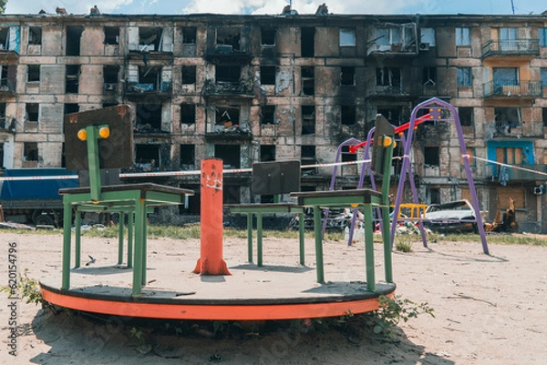 Fototapeta An empty children's playground next to a residential building destroyed by rocket fire. War in Ukraine. Terror of the civilian population
