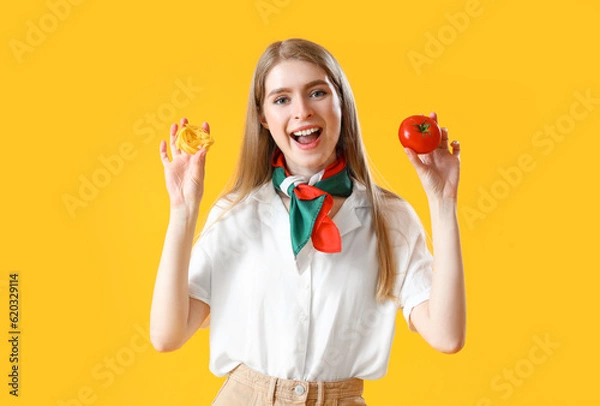 Fototapeta Young woman with raw pasta and tomato on yellow background