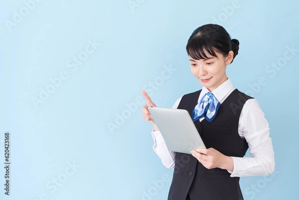 Fototapeta タブレットを操作するベストにリボンタイの制服を着た、受付業務、事務業務の女性