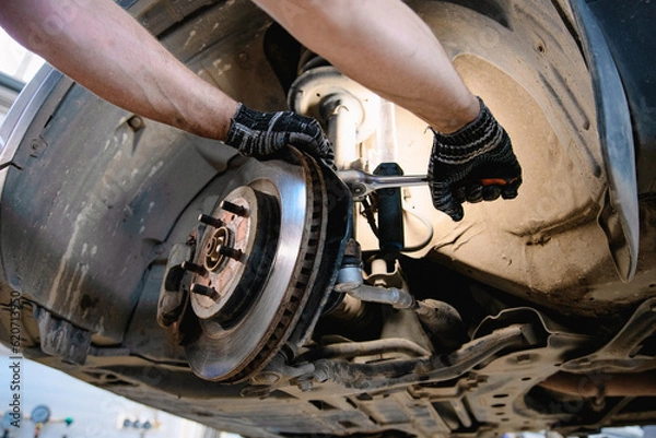 Fototapeta The hands of a mechanic hold a tool. Repair of the brake system of a car with a shallow depth of field