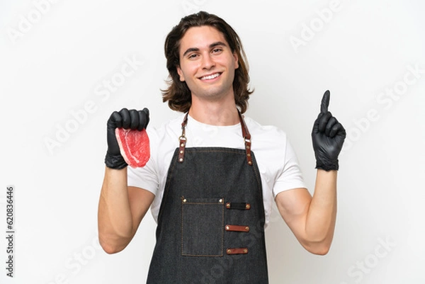 Fototapeta Butcher handsome man wearing an apron and serving fresh cut meat isolated on white background showing and lifting a finger in sign of the best