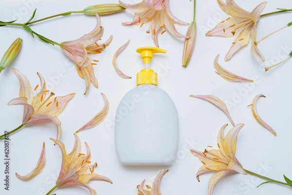 Fototapeta Cosmetic plastic bottle with dispenser liquid soap, hand cream on white background with pink, yellow lily flowers with an empty space for text, copy space, flat lay, body care concept organic product