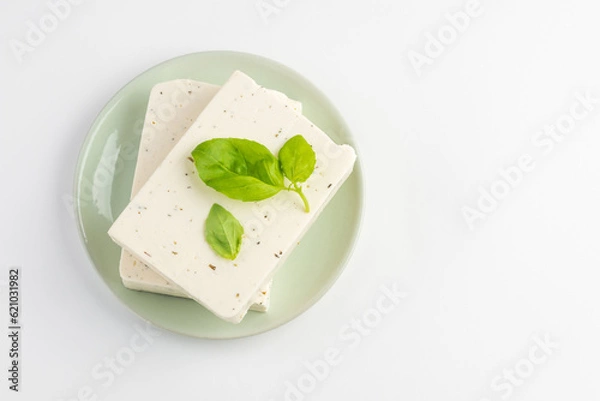 Fototapeta Top view of  tofu, paneer or soy cheese with fresh basil leaves in a green plate isolated with copy space