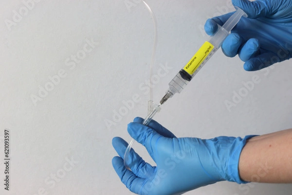 Fototapeta Profissional wearing gloves holding a ketamine syringe drug with liquid and injecting the drug in the intravenous acess.