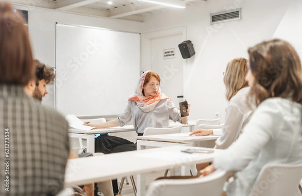 Fototapeta Ginger, muslim, female employee checking her phone while having a meeting at the classroom