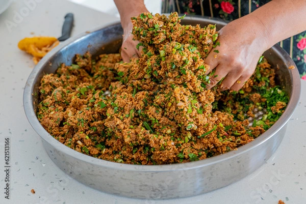 Fototapeta A woman kneading a local dish made with bulgur, tomato paste and greens with her hands