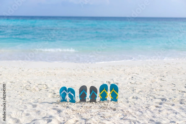 Fototapeta Three pairs of flip flops on the beach on the background of ocean in the Maldives. Family vacation