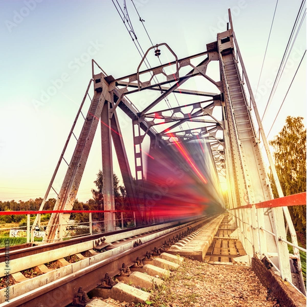 Fototapeta Highspeed train moves fast on the bridge at sunsset.