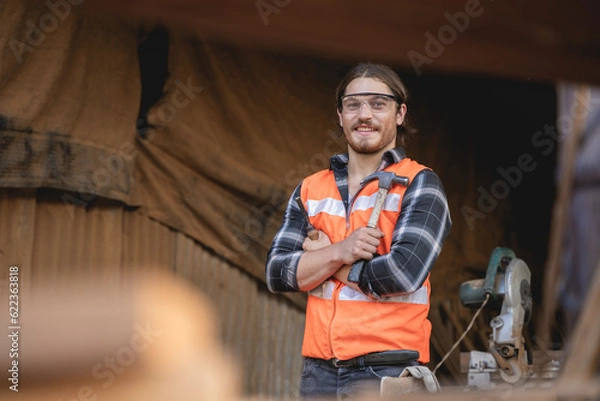Fototapeta Young male carpenter working on design and cutting wood in the workshop, using a circular saw to cut a large board of wood on a wooden table in the workshop