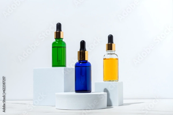 Fototapeta Face serum dropp bottles on white podiums on white background. Home routine skin care cosmetic set. Unbranded bottles for your design.