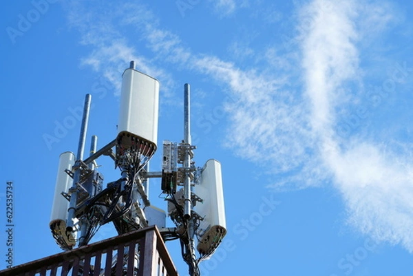Fototapeta Telecommunication tower of 4G and 5G cellular. Macro Base Station. 5G radio network telecommunication equipment with radio modules and smart antennas mounted on a metal against cloulds sky background.
