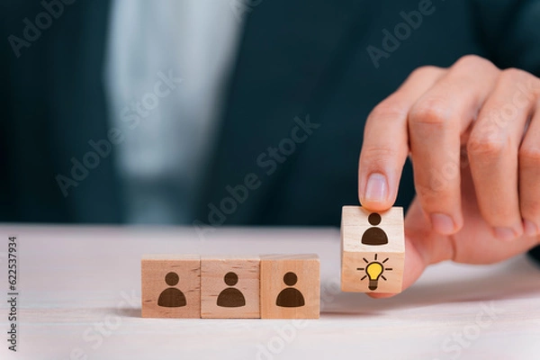 Fototapeta Leader choosing the best new idea with light bulb icon on wooden blocks. Explore creative design, solutions, strategy reviews. Inspiring innovation and teamwork.