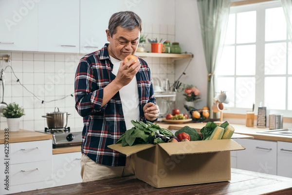 Obraz The retired Asian man enjoyed the convenience of online shopping as he unpacked a carton box filled with healthy vegetable ingredients on his dining table.