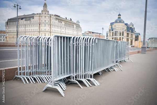 Fototapeta Folded portable temporary fence parts on sidewalk. Preparation for roads and sidewalk closing in case of possible protests or mass events and a large crowd of people.