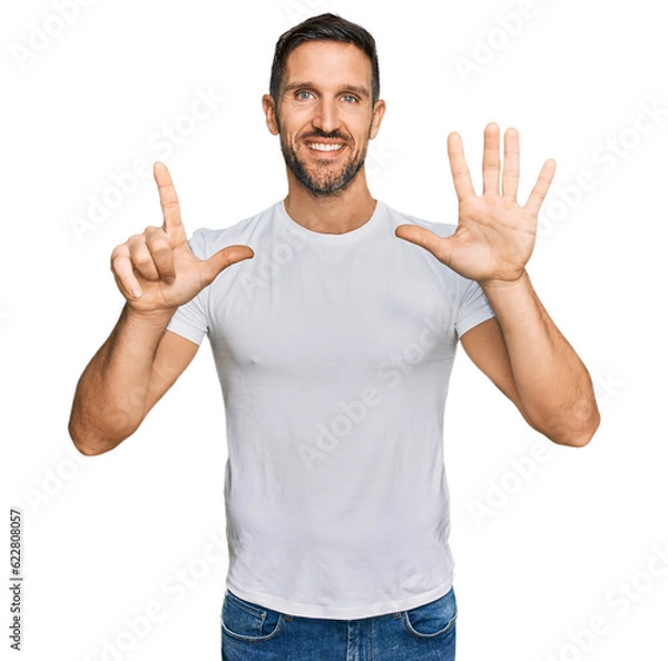 Fototapeta Handsome man with beard wearing casual white t shirt showing and pointing up with fingers number seven while smiling confident and happy.