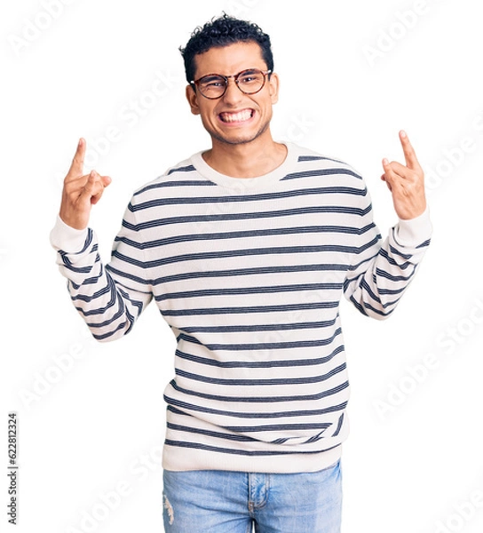 Obraz Hispanic handsome young man wearing casual clothes and glasses shouting with crazy expression doing rock symbol with hands up. music star. heavy concept.