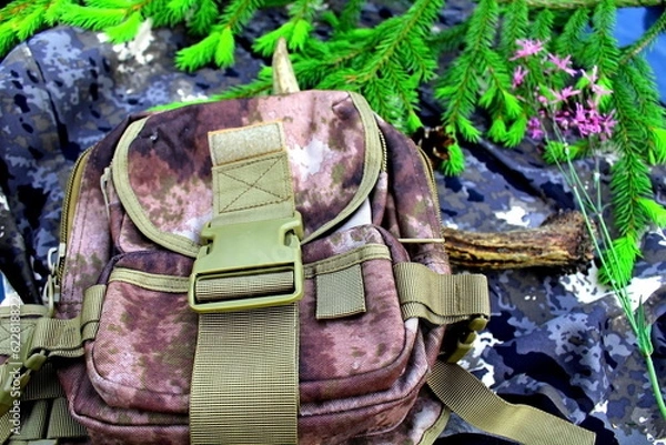 Fototapeta Equipment for outdoor travel on camouflage fabric with branches of coniferous trees