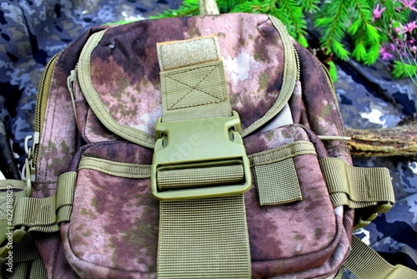 Fototapeta Equipment for outdoor travel on camouflage fabric with branches of coniferous trees