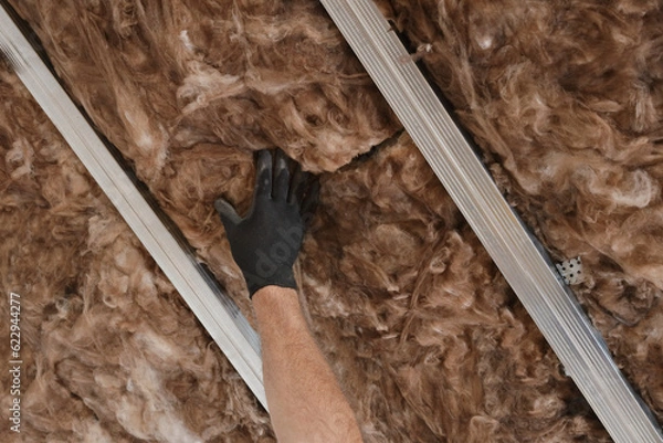 Fototapeta Closeup of worker hand in glove placing  mineral wool insulation for energy efficiency to ceiling with aluminum construction