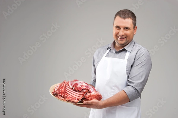Obraz professional butcher smiling and holding raw meat.
