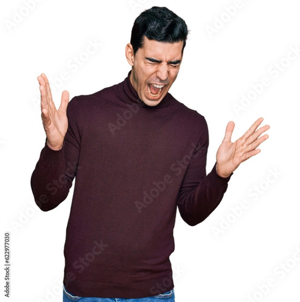 Fototapeta Handsome hispanic man wearing casual turtleneck sweater celebrating mad and crazy for success with arms raised and closed eyes screaming excited. winner concept