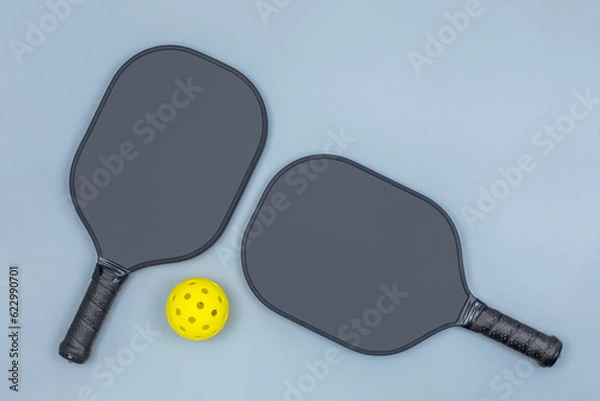 Obraz Closeup top view of two black pickleball paddles and a yellow ball on light gray background with copy space