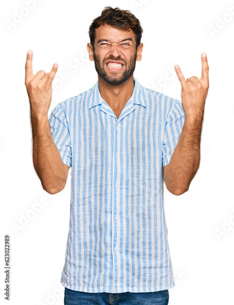 Fototapeta Handsome young man with beard wearing casual fresh shirt shouting with crazy expression doing rock symbol with hands up. music star. heavy concept.
