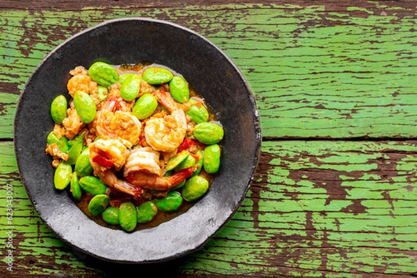 Obraz Pad Ped Sator Goong, Thai food, Shrimps and Stink Beans Fried in Red Curry Paste in wabi sabi plate on green wood texture background, top view, Pakria, Bitter bean, Twisted cluster bean, Stink bean