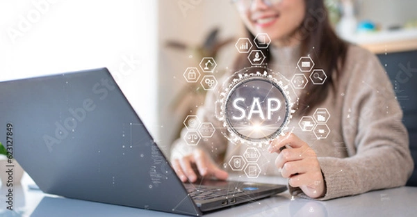 Obraz System Applications and Product (SAP). Program helps manage business to access information quickly accurately. Woman using laptop holding magnifying glass with SAP text inside. An icon on background.