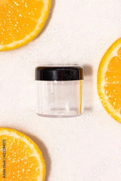 Fototapeta Frasco transparente con tapa negra sin etiqueta en agua con fondo blanco y naranjas partidas