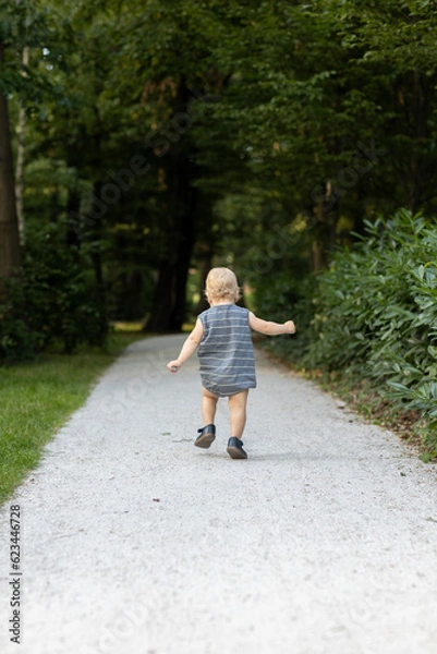 Fototapeta Little boy running on the road in the park. Summer time.