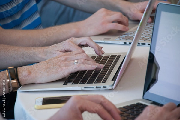 Fototapeta Female hands typing on a laptop computer with a phone by the side 