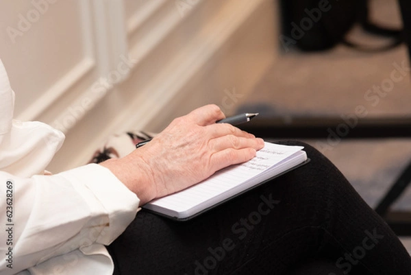 Fototapeta Hand holding a pen on top of a notebook taking notes