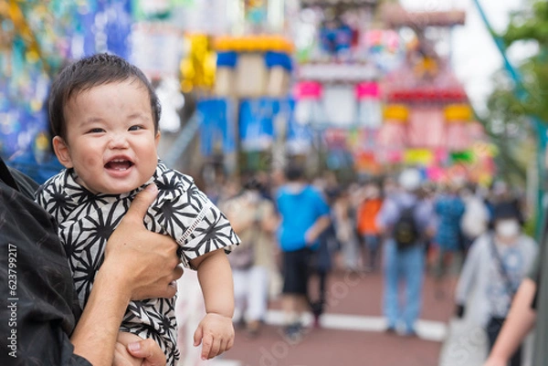 Fototapeta 夏祭りで七夕飾りを見て笑顔になる甚平姿の生後9か月の赤ちゃんと抱っこする浴衣姿のパパ