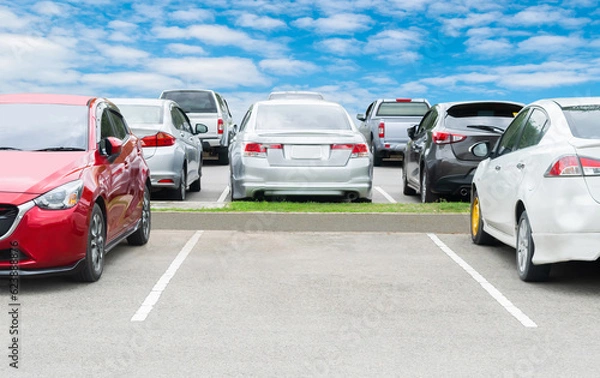 Fototapeta Cars parking in a row in stock background. Vehicle transportation trip inventory merchandise. Car parked in large asphalt parking lot with white cloud and blue sky background. Outdoor parking lot