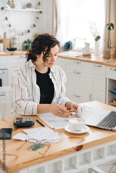 Obraz Focused caucasian woman working at home in the kitchen with financial papers, counting on a calculator, paying bills, planning a budget to find a way to save money. Self-employed accounting