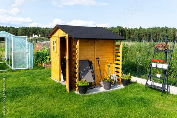 Obraz A wooden garden shed standing on a concrete foundation in a garden, flowers and tools visible.