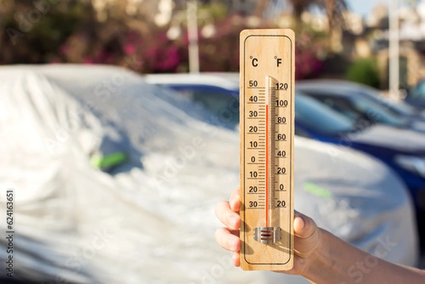 Fototapeta Hot weather. Thermometer in hand in front of covered car on tne street  during heatwave. High temperature concept